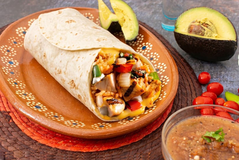 A large burrito filled with chicken, rice, cheese, and vegetables on a decorative plate.